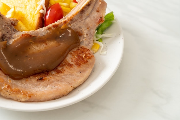 Os Benefícios da Carne Suína: Corte e Preparação 1 Um Bife De Costeleta De Porco Servido Com Batatas Fritas Douradas E Uma Pequena Salada Em Um Prato Branco.