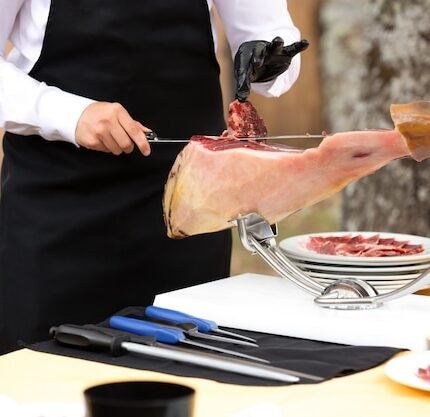 Uma Cena De Açougue Com Uma Pessoa Usando Luvas Fatiando Fatias Finas De Presunto Ibérico Durante Uma Celebração.