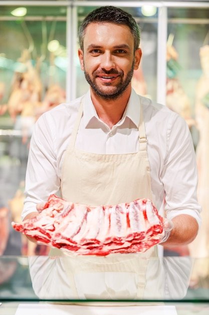 Um Jovem Açougueiro Sorrindo E Segurando Um Pedaço De Carne Fresca Enquanto Está Na Caixa Do Supermercado.