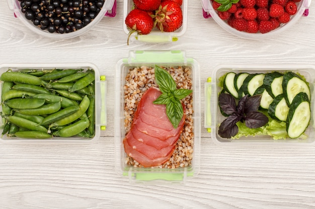Carnes para o Dia a Dia: Opções Práticas do Açougue do Nilo 1 Vista De Cima De Recipientes Plásticos Para Preparo De Refeições Cheios De Trigo Sarraceno Cozido, Fatias De Carne, Pepinos Frescos, Ervilhas Verdes E Uma Salada Colorida, Contra Um Fundo Cinza.